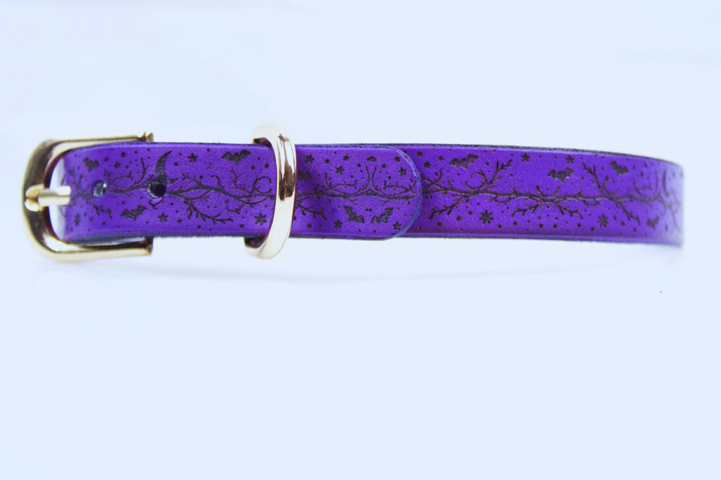A purple leather belt with a gold buckle, featuring a pattern of stars and bats on the surface.