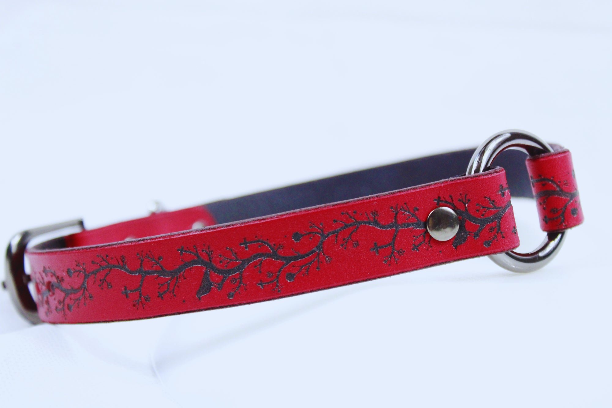 A red leather dog collar with a black tree branch design on it.
