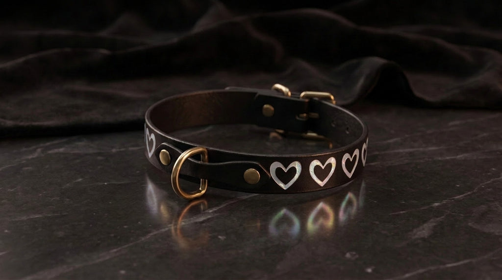 A black leather collar with white heart-shaped designs on it, resting on a dark surface.