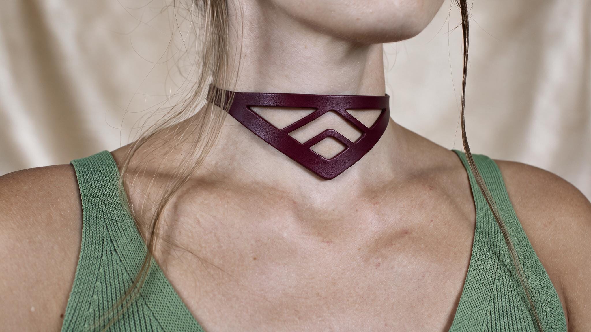 A close-up of a woman wearing a green top and a burgundy choker necklace with a geometric pattern.