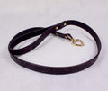 A purple leather leash with a gold heart-shaped tag attached, lying on a white surface.