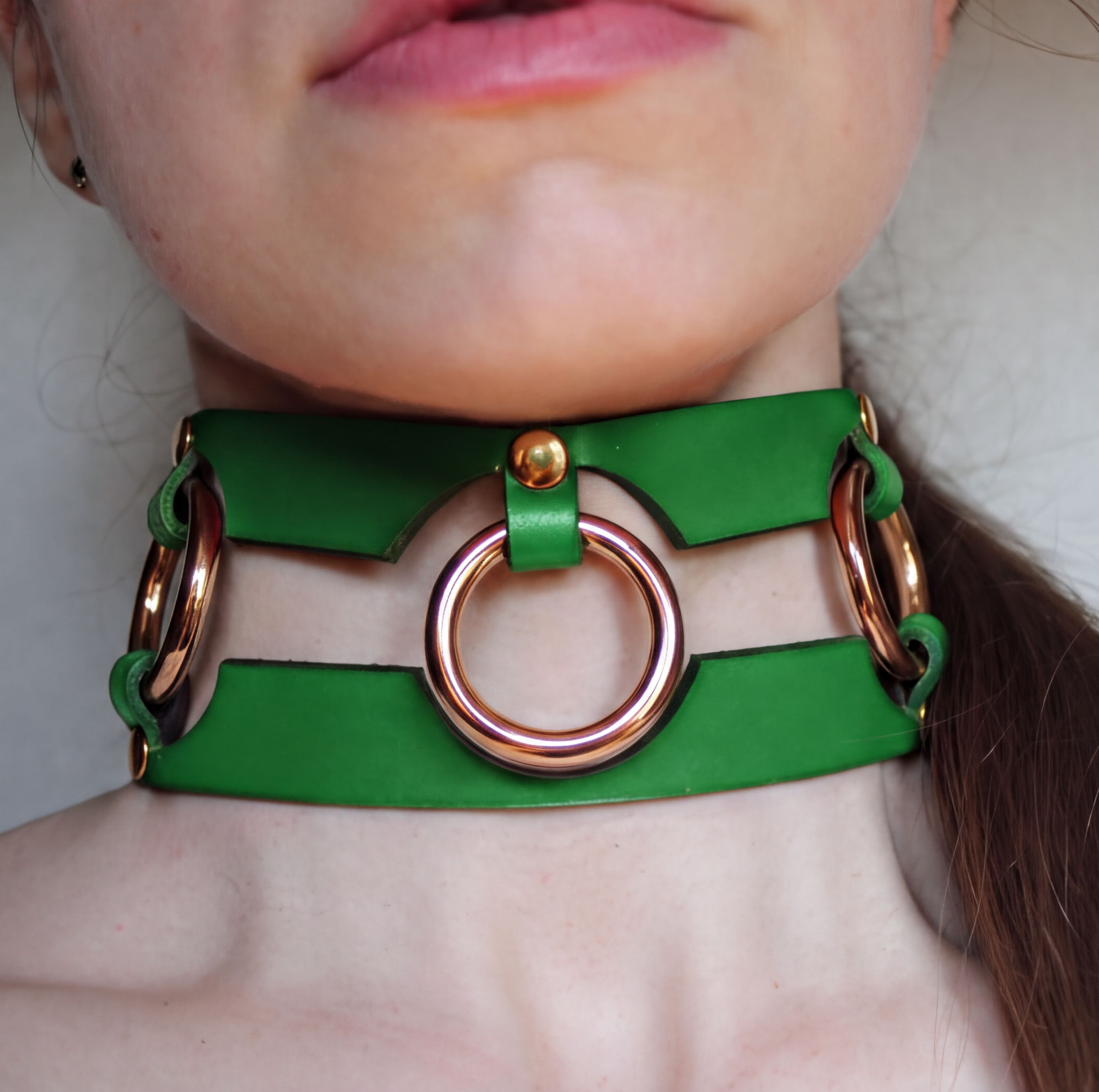 A close-up of a person's neck wearing a green leather choker necklace with three circular metal rings.