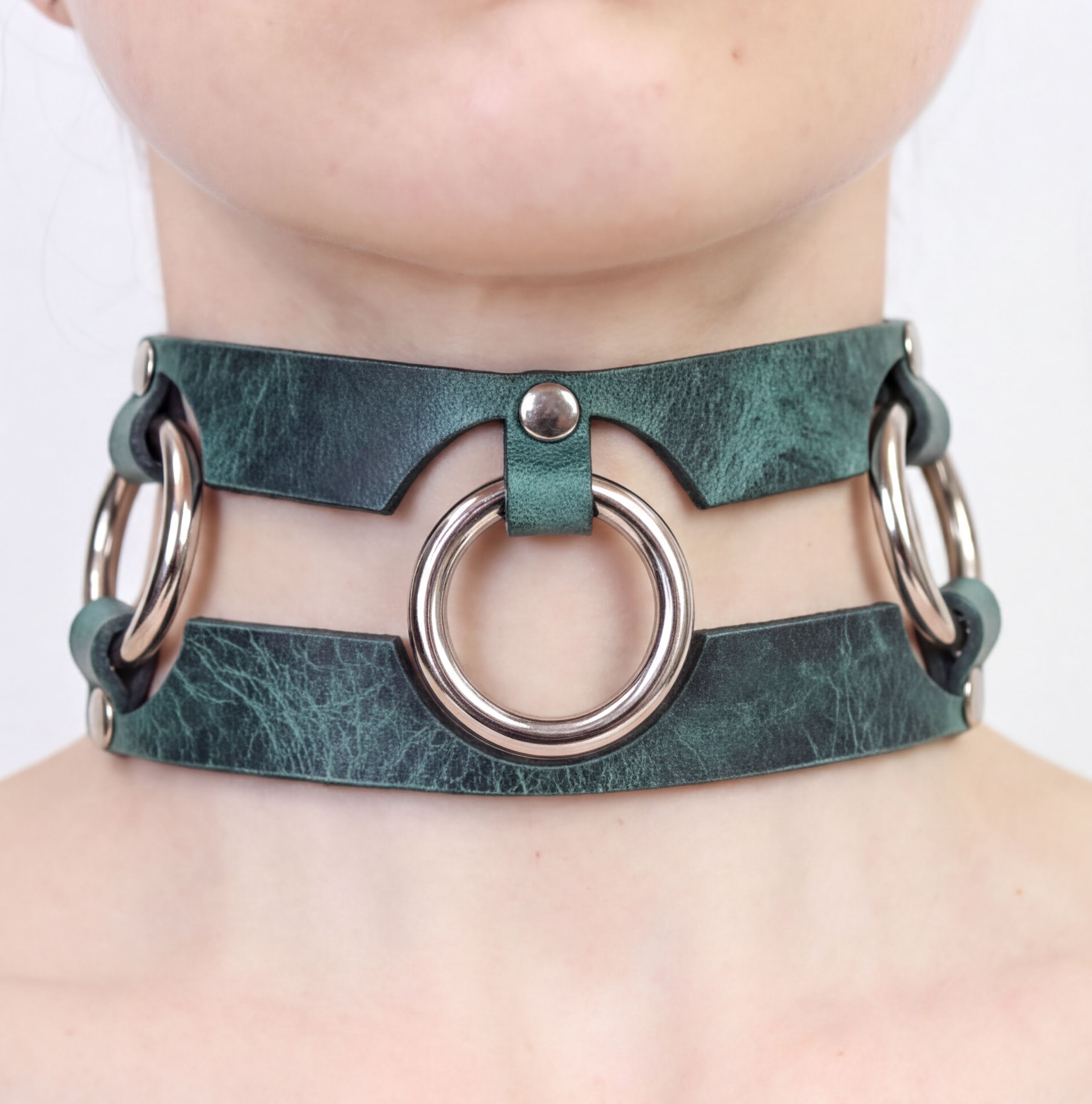 A close-up of a person's neck wearing a green leather choker necklace with metal rings.