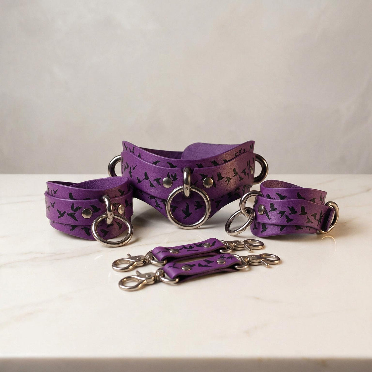 a collection of purple leather straps with metal rings and buckles, arranged on a white surface.