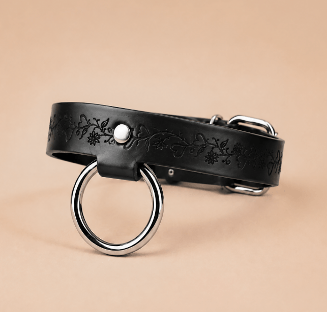 A black leather collar with a metal ring and a floral design on the strap.