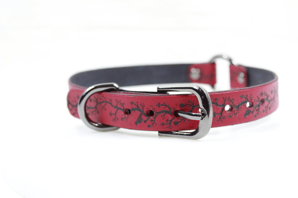 A red leather dog collar with a black tree branch design on it.