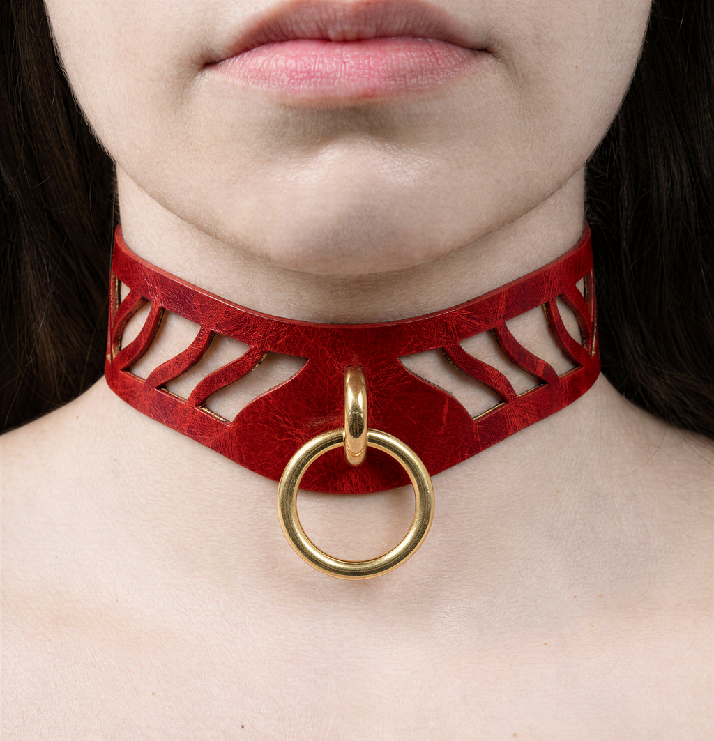 A close-up of a person's neck and chest area wearing a red choker necklace with a gold ring.