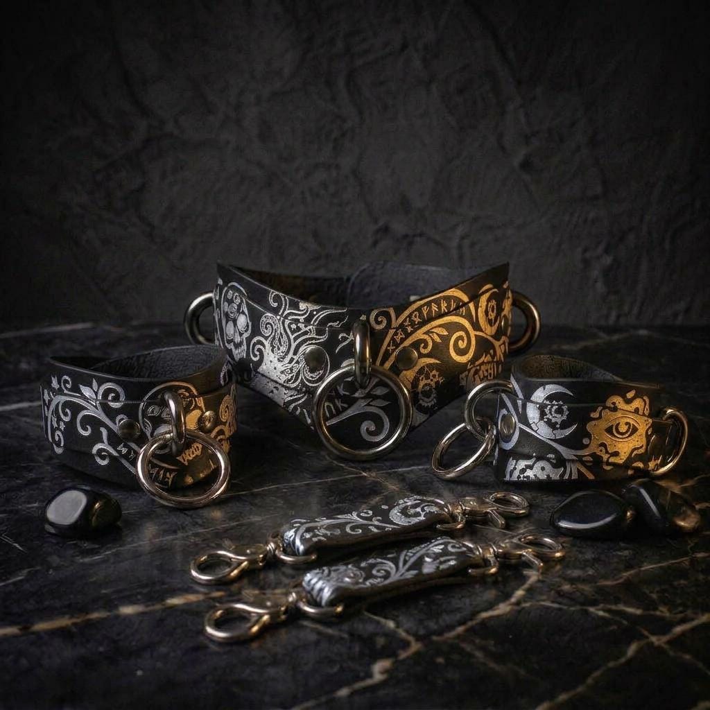 a collection of ornate leather straps with intricate designs, including a central ornate strap and several smaller straps with similar designs. The straps are displayed on a dark surface, with some small stones or pebbles scattered around them.