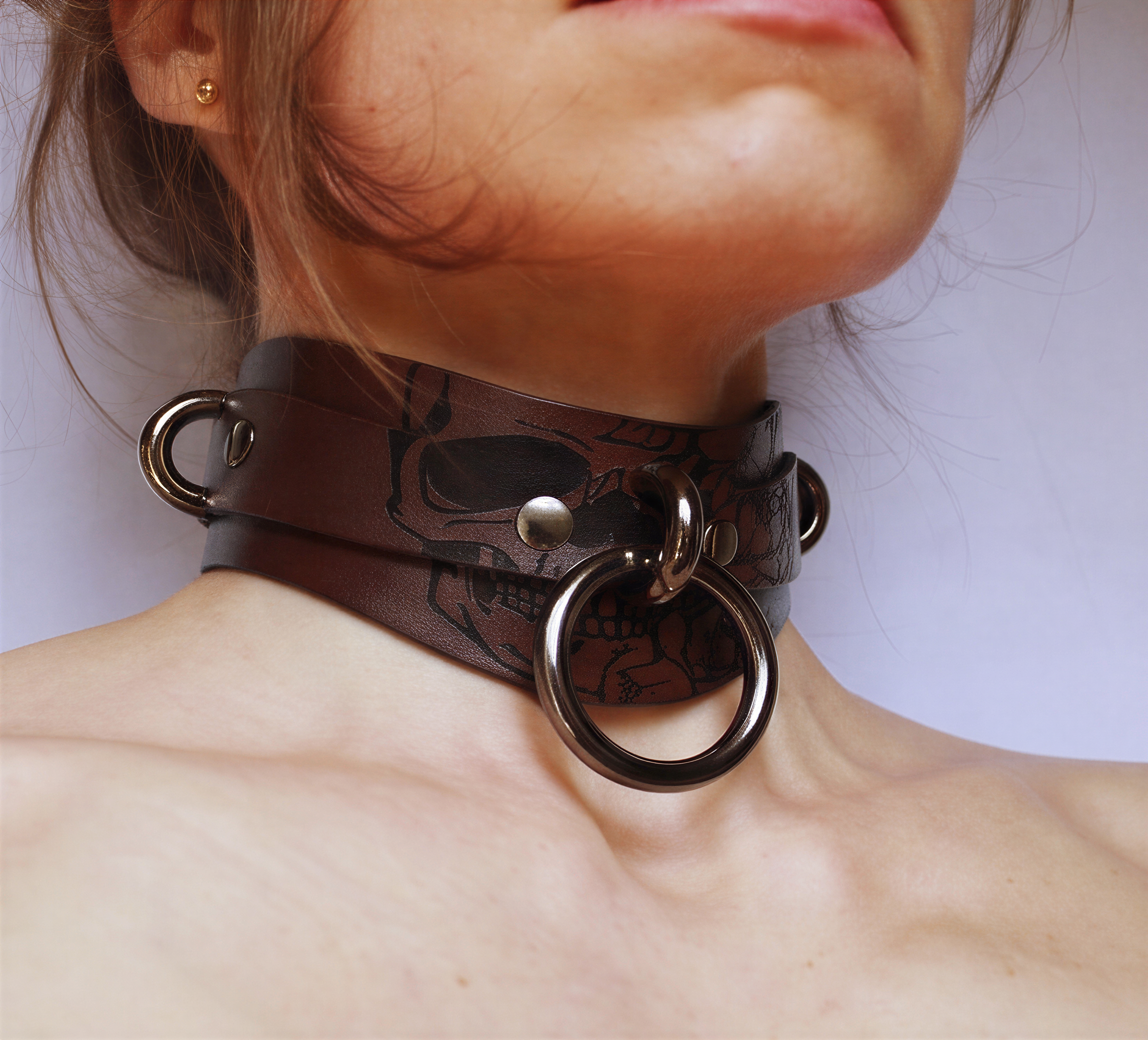 A close-up of a person's neck wearing a leather choker necklace with a skull design and metal rings.