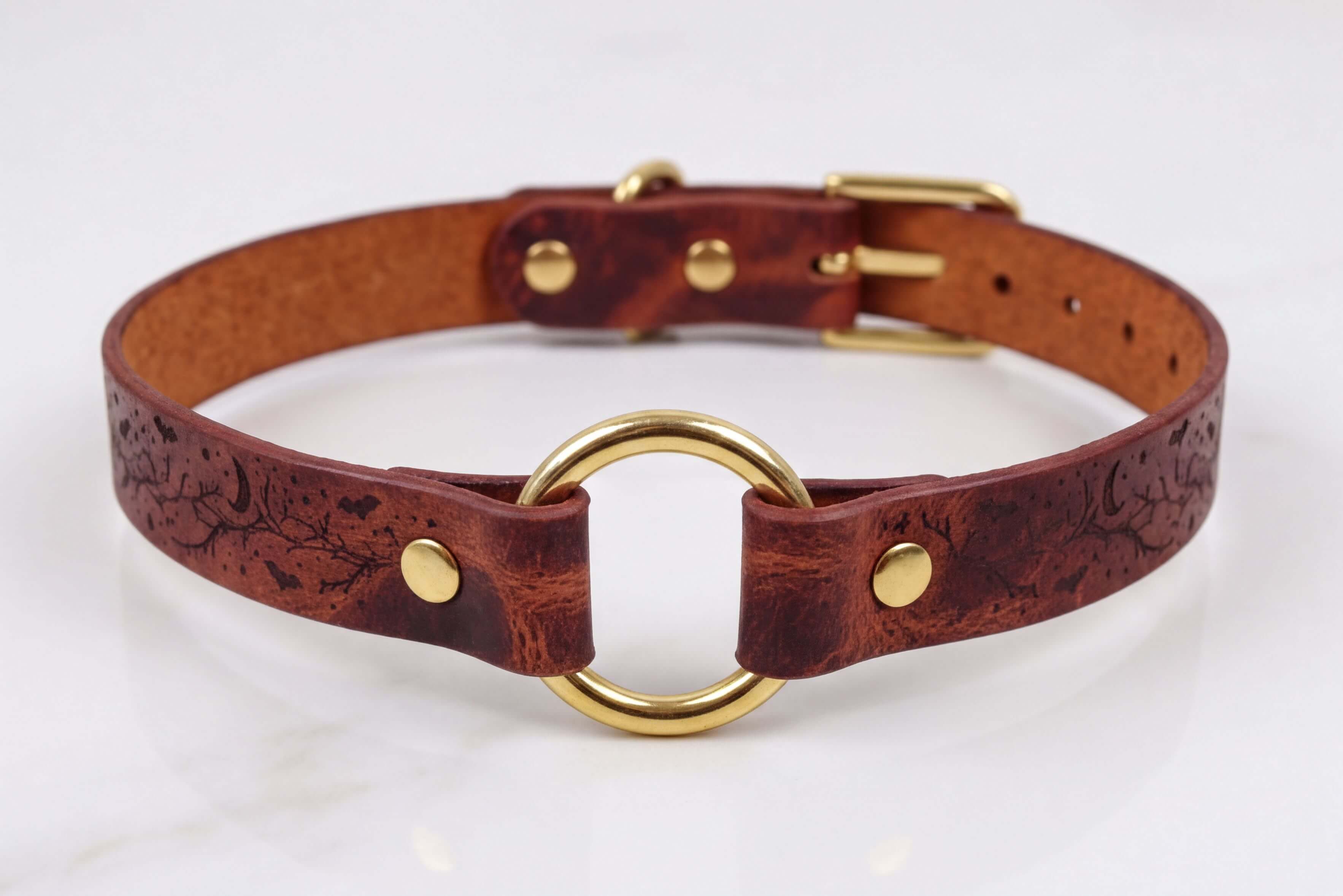 A brown leather choker collar with a gold-colored metal ring and buckle.