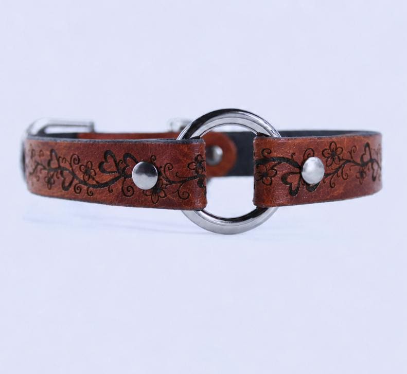 A brown leather collar with a metal ring and floral designs.