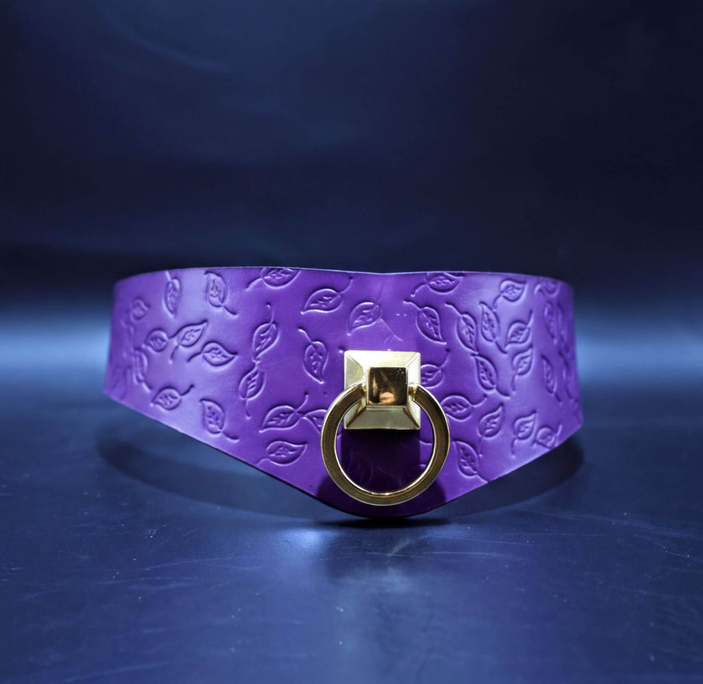 A purple leather choker necklace with a gold-colored metal ring and a leaf pattern design.