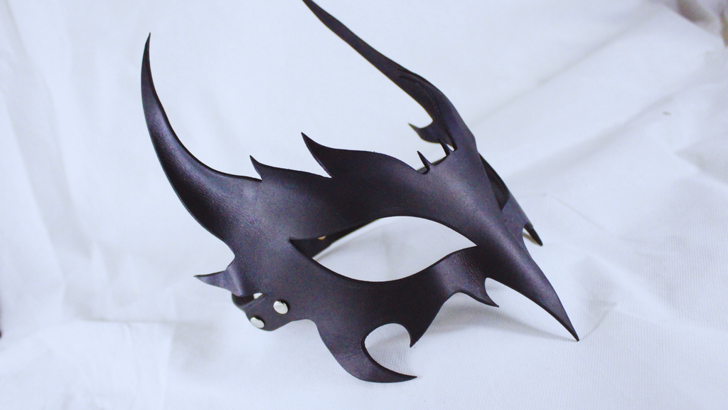 A black, sculpted mask with sharp, pointed edges and a dark, textured surface.