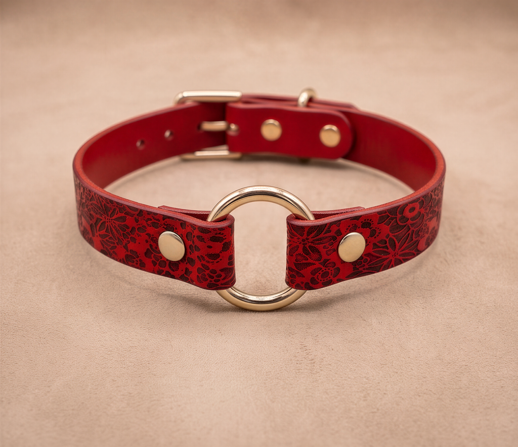 A red leather collar with a gold ring and buckle, featuring a floral pattern.