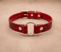 A red leather collar with a gold ring and buckle, featuring a floral pattern.
