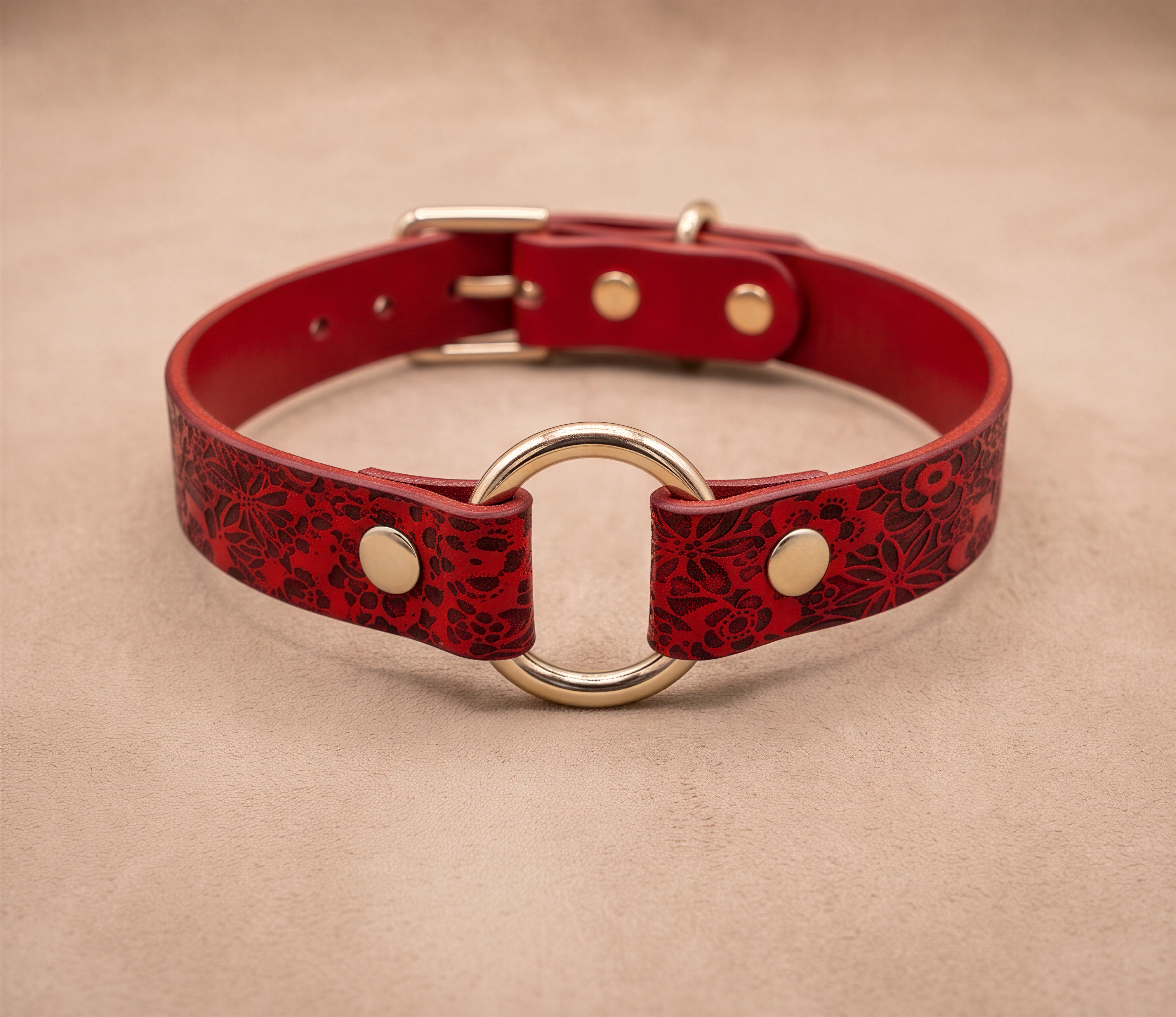 A red leather collar with a gold ring and buckle, featuring a floral pattern.