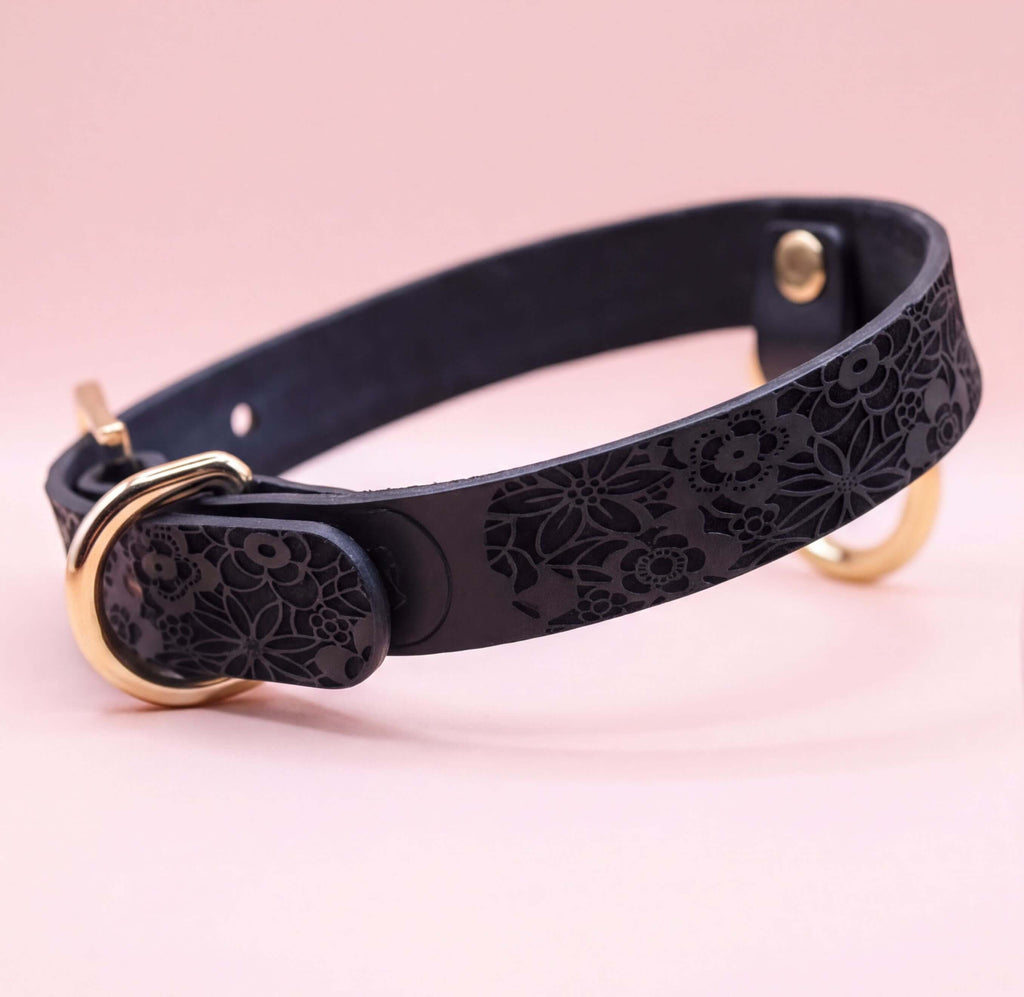 A black leather collar with a floral pattern and a gold buckle.