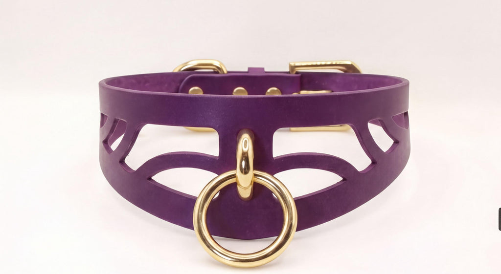 A purple leather choker necklace with a gold-colored metal ring and a cutout design on the front.