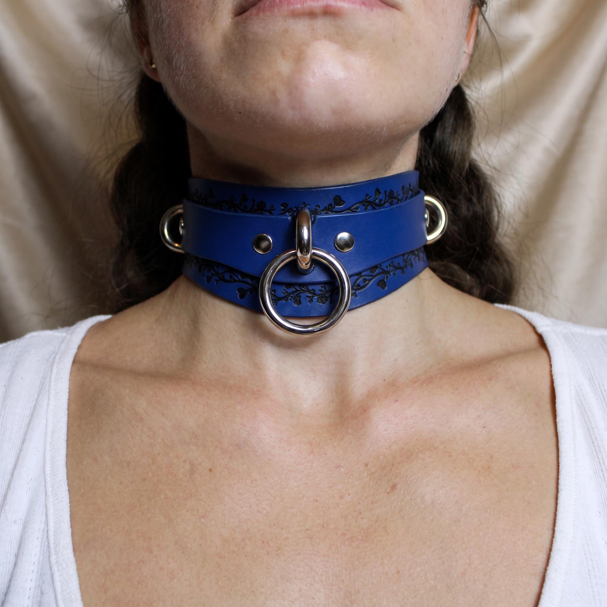 A close-up of a person wearing a blue leather choker necklace with a metal ring.