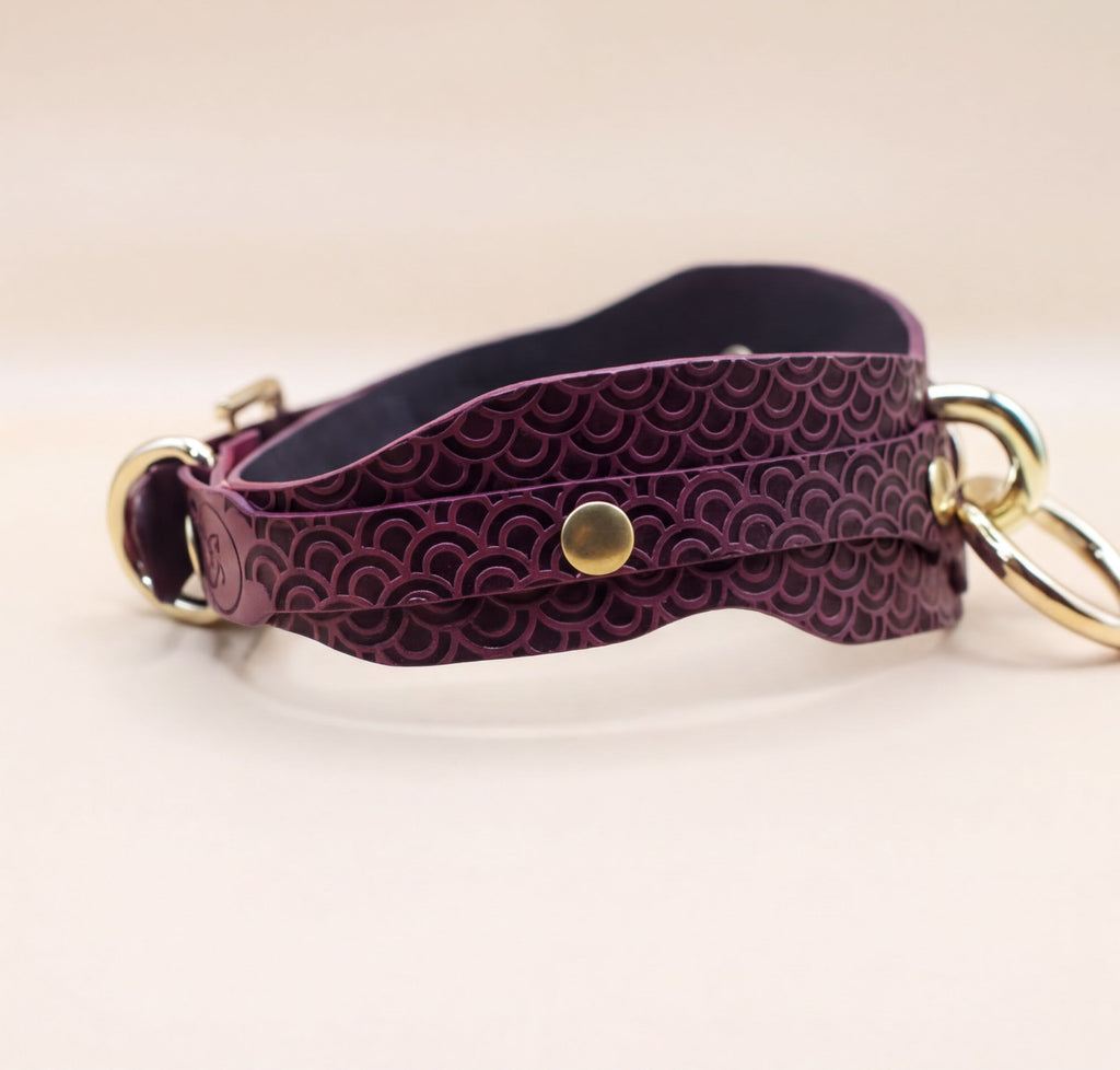 A burgundy leather choker necklace with a metallic buckle and two gold-colored rings.