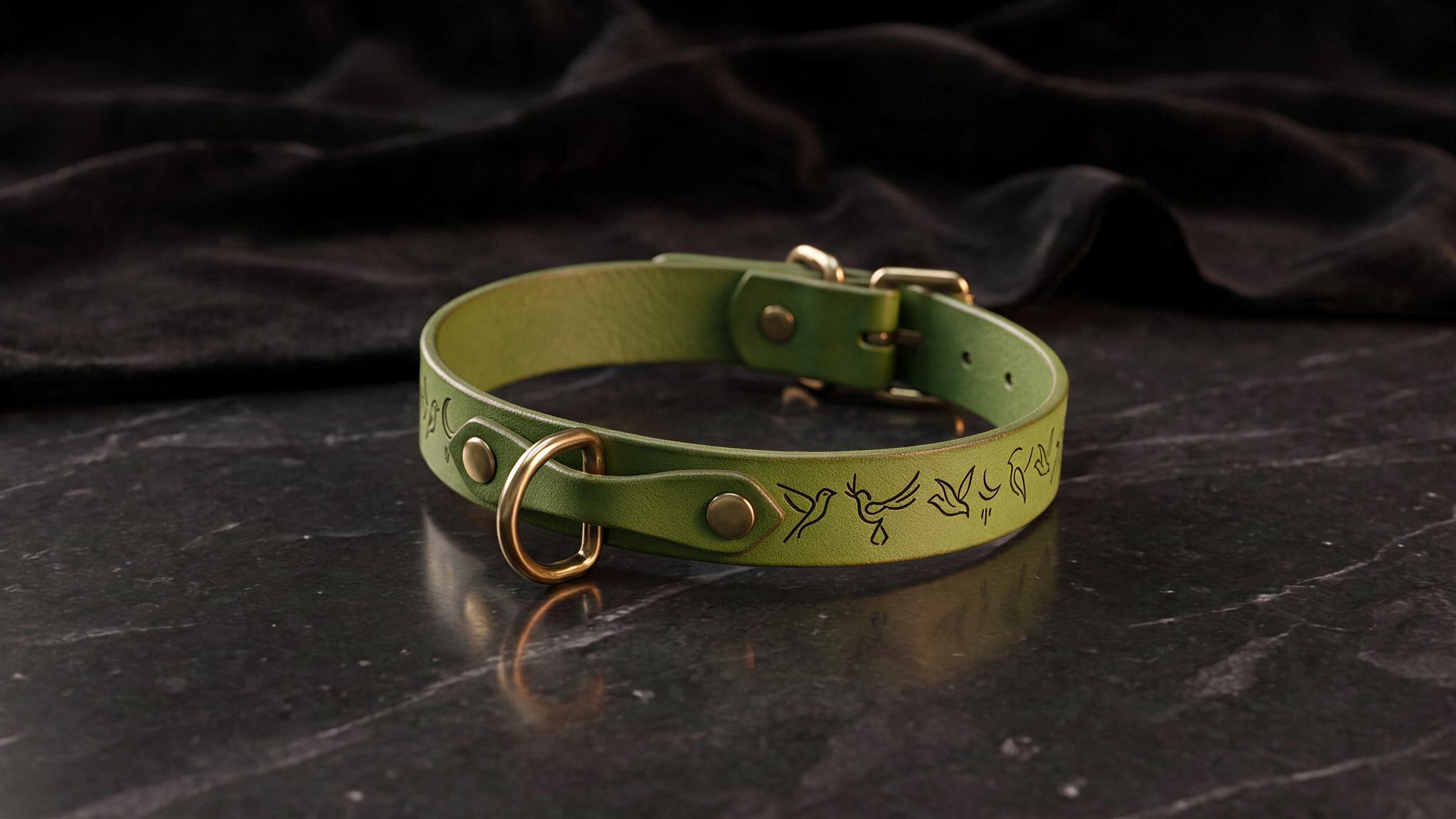 A green leather collar with a gold buckle and a bird design on it, resting on a black marble surface.