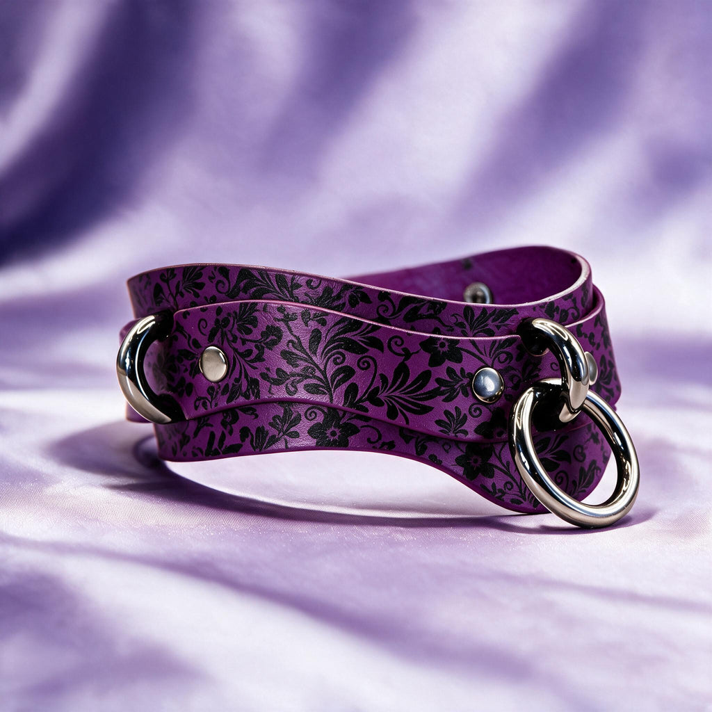 A purple leather choker necklace with a floral pattern and metal rings on the ends, resting on a purple fabric background.