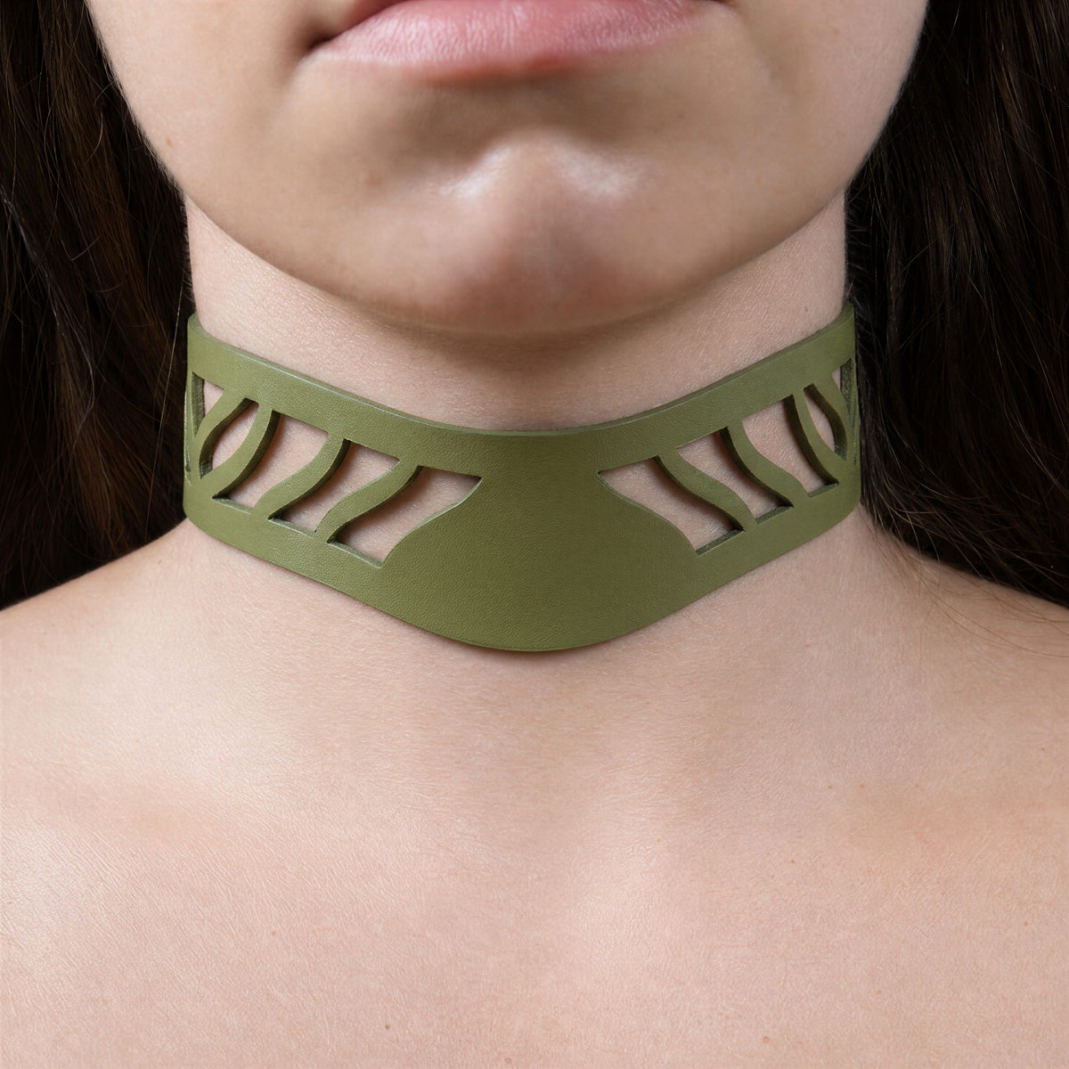 A close-up of a person's neck and chest area wearing a green choker necklace with a unique cutout design.