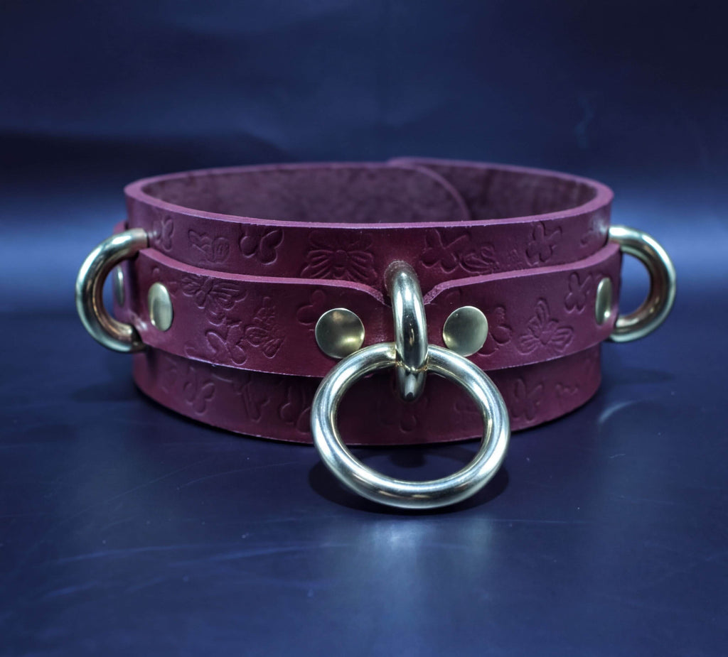 A burgundy leather choker necklace with gold metal rings and a metal clasp.