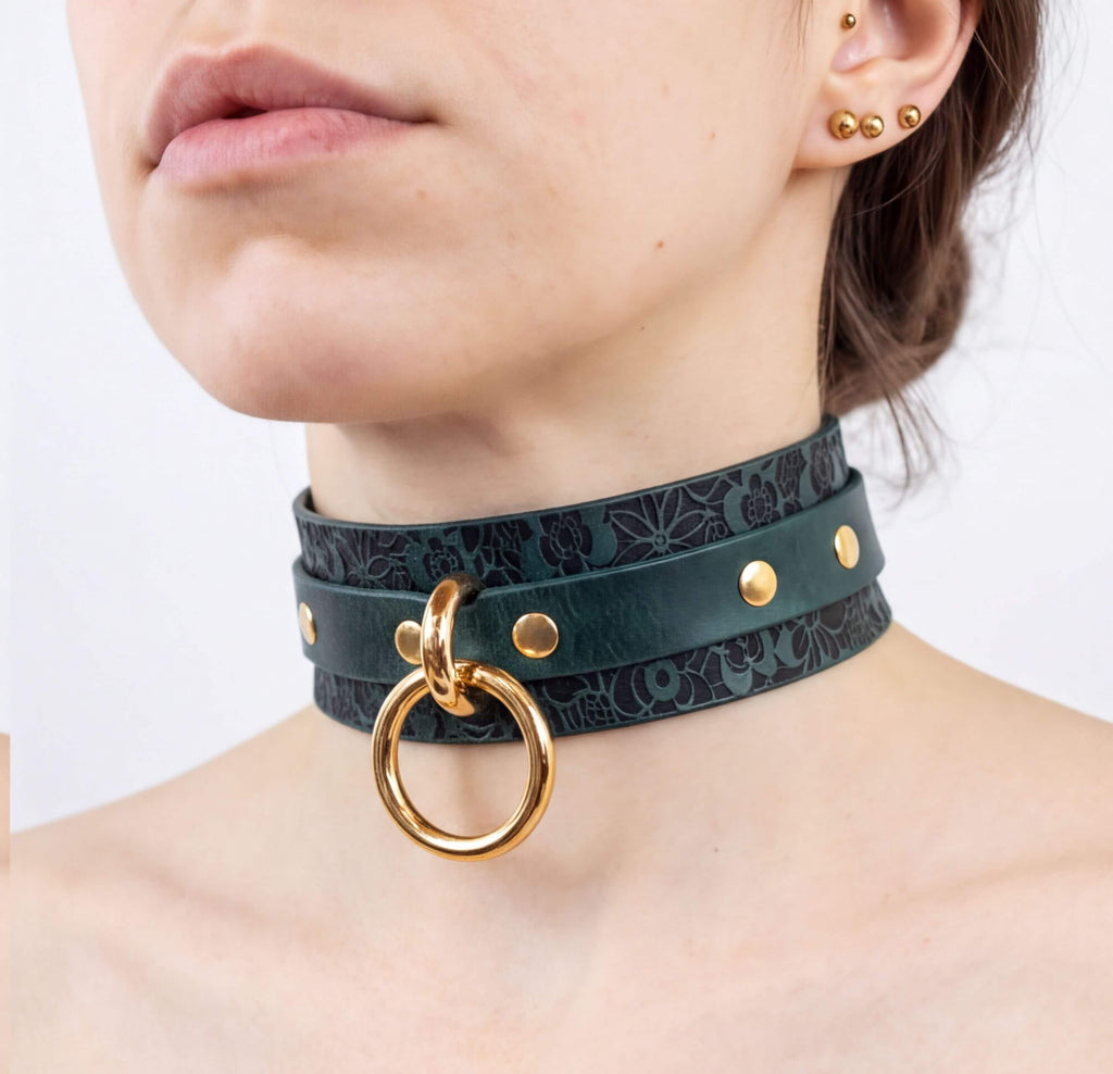 A close-up of a woman's neck and chest area, featuring a dark green choker necklace with a gold ring and studs.