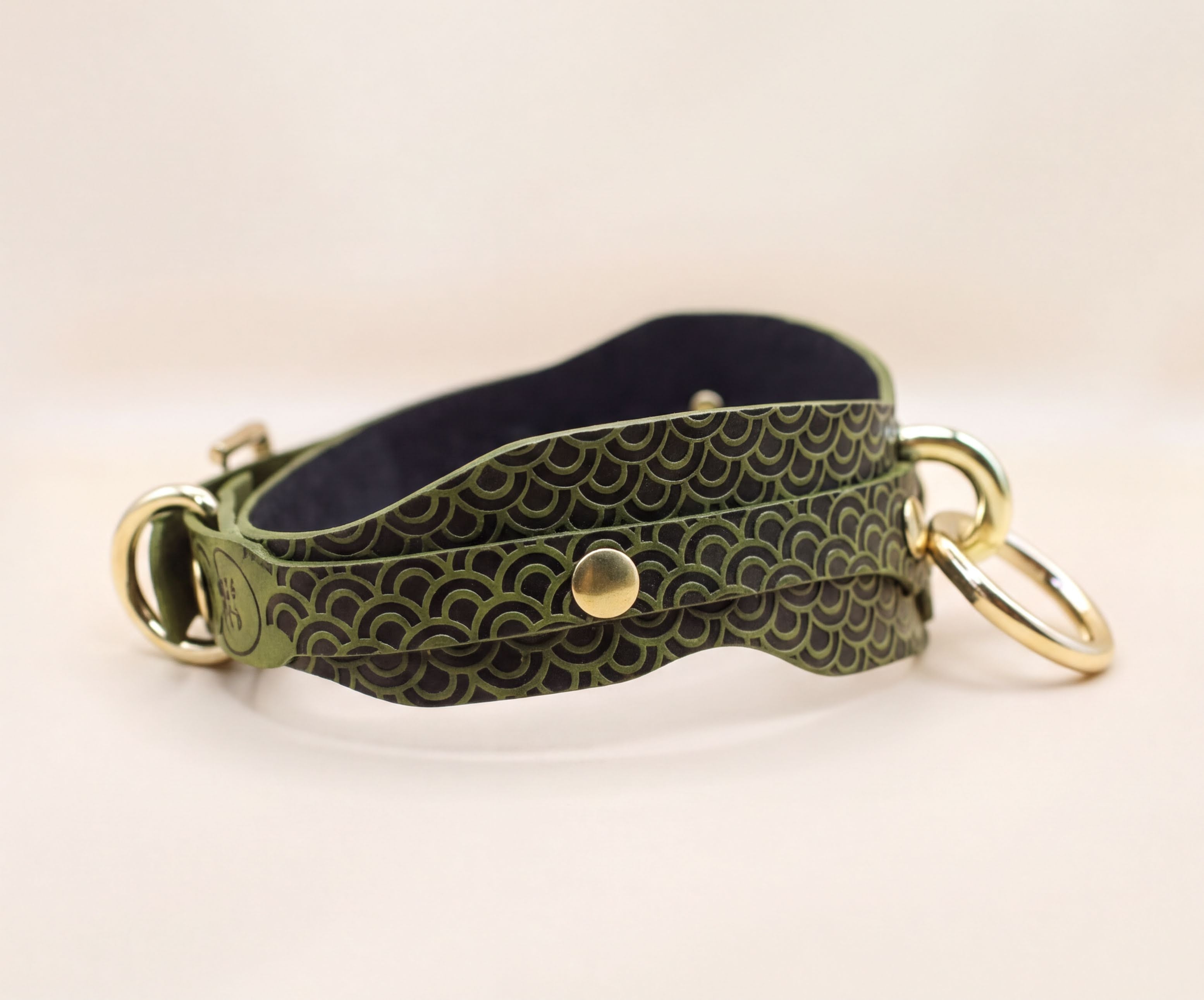 A green and black patterned leather collar with gold-colored metal rings and a buckle.