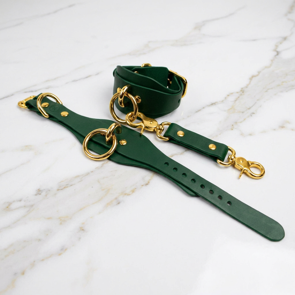 a pair of green leather straps with gold-colored metal rings and buckles, placed on a marble surface.