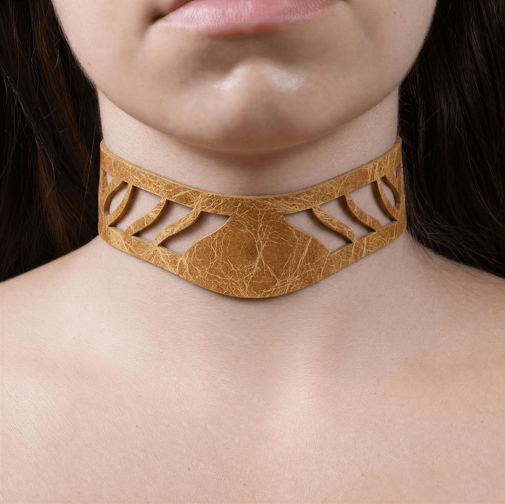 A close-up of a person's neck and chest area wearing a gold-colored choker necklace with a cutout design.