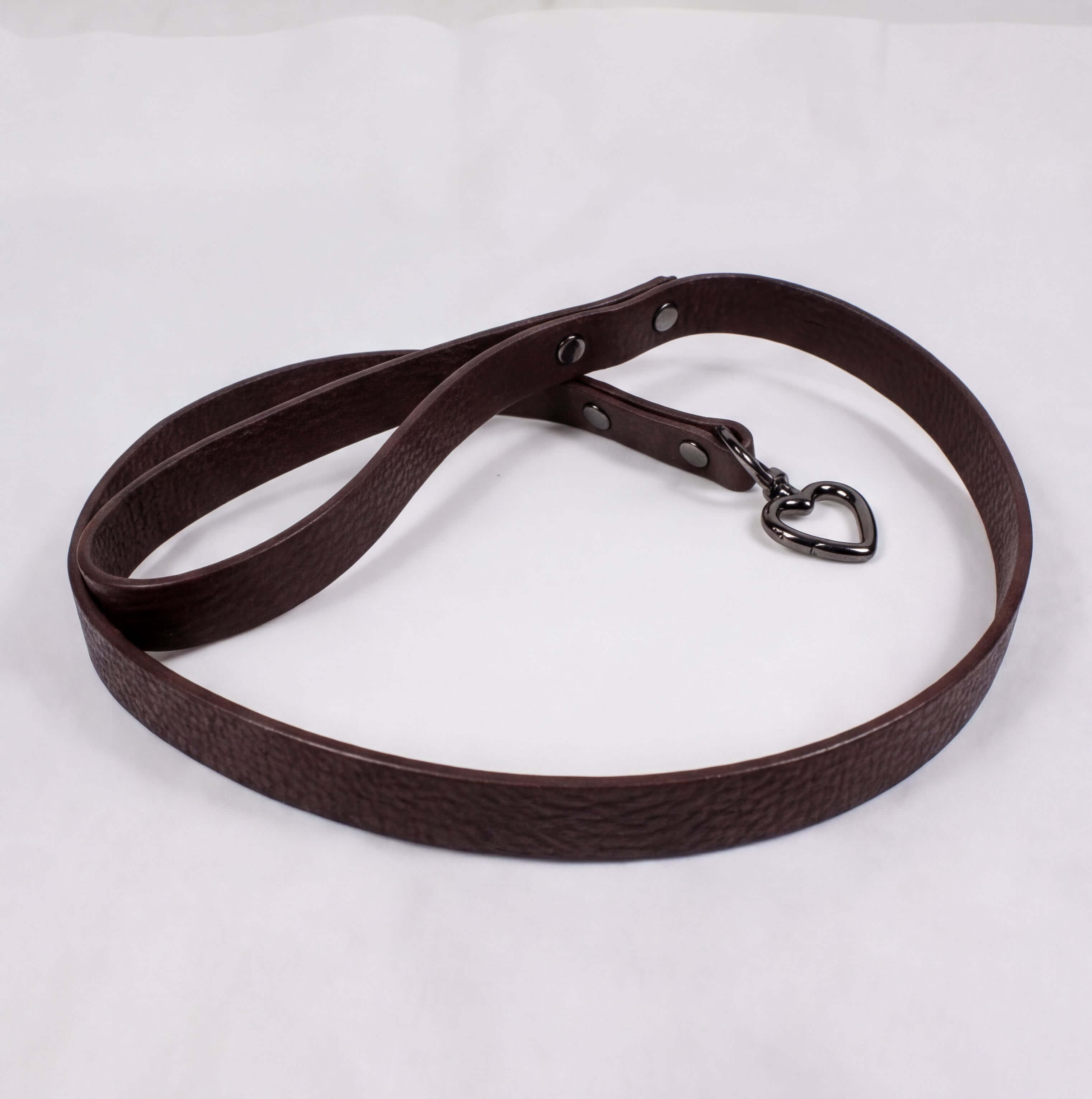 A brown leather dog leash with a heart-shaped charm attached.