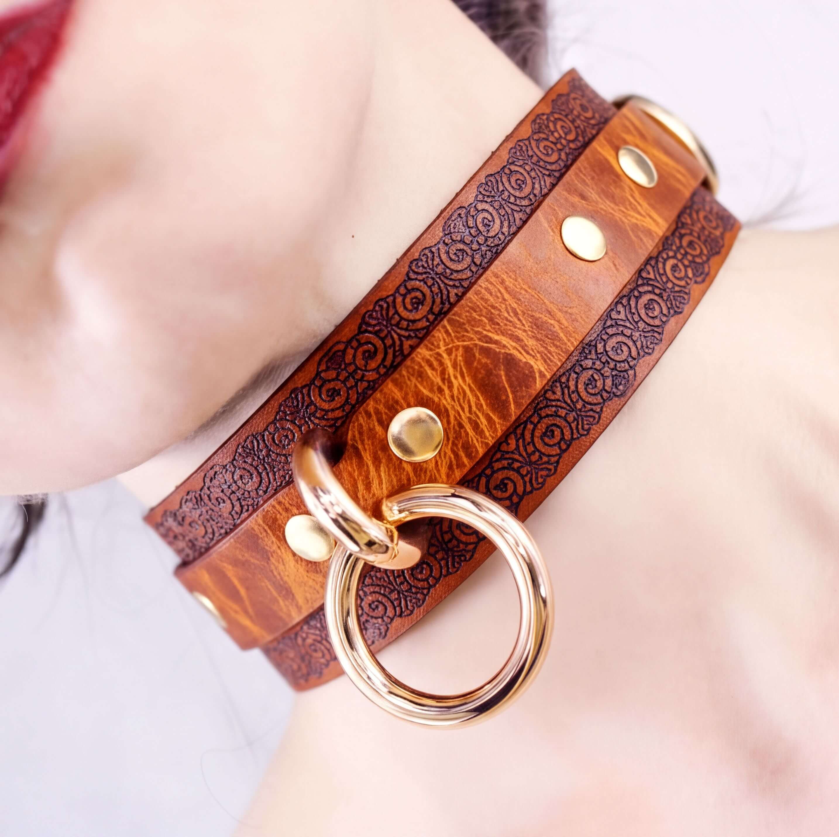A close-up of a leather choker necklace with a metal ring and decorative elements.