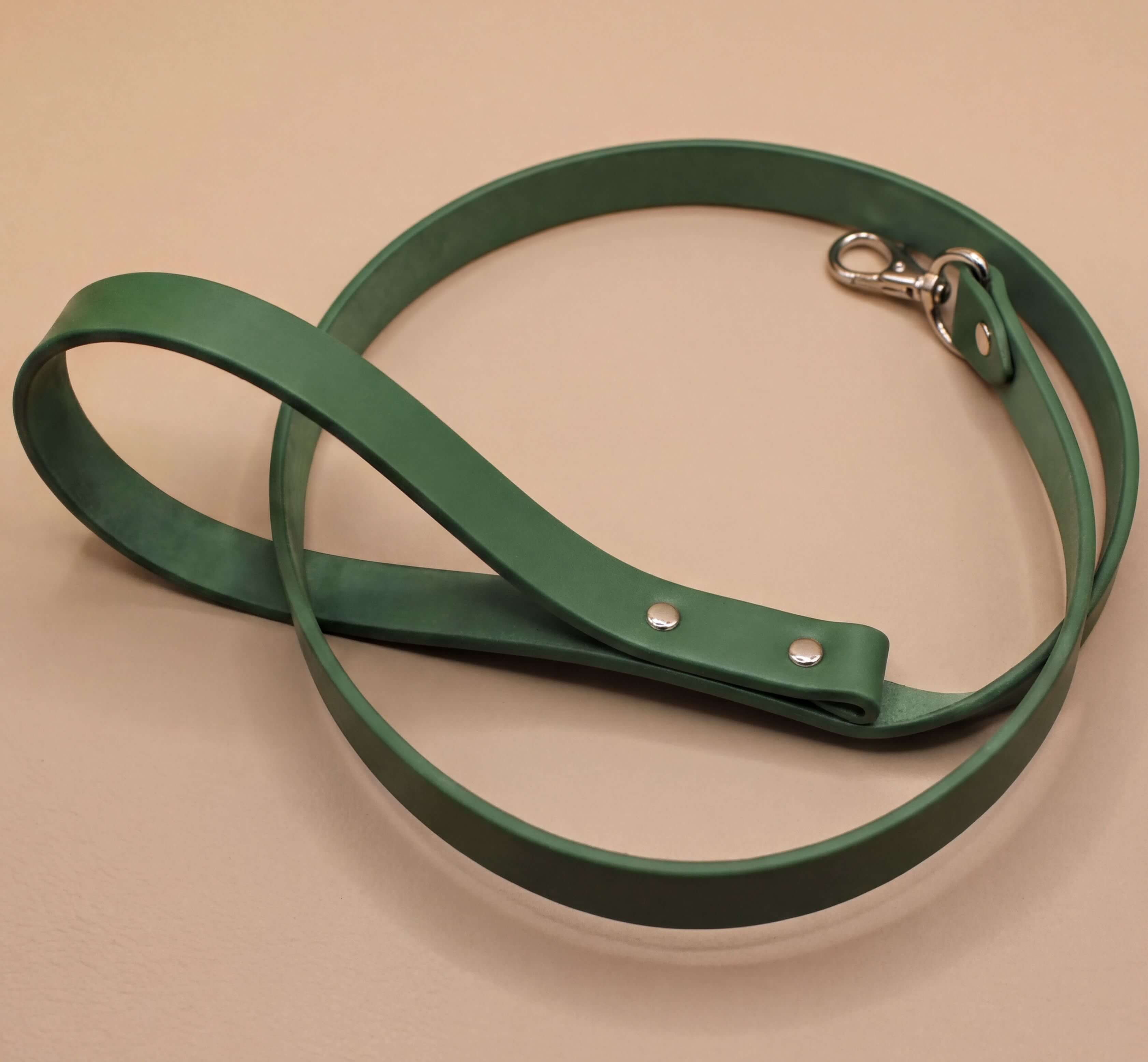 A green leather dog leash with a metal attachment is shown on a beige surface.