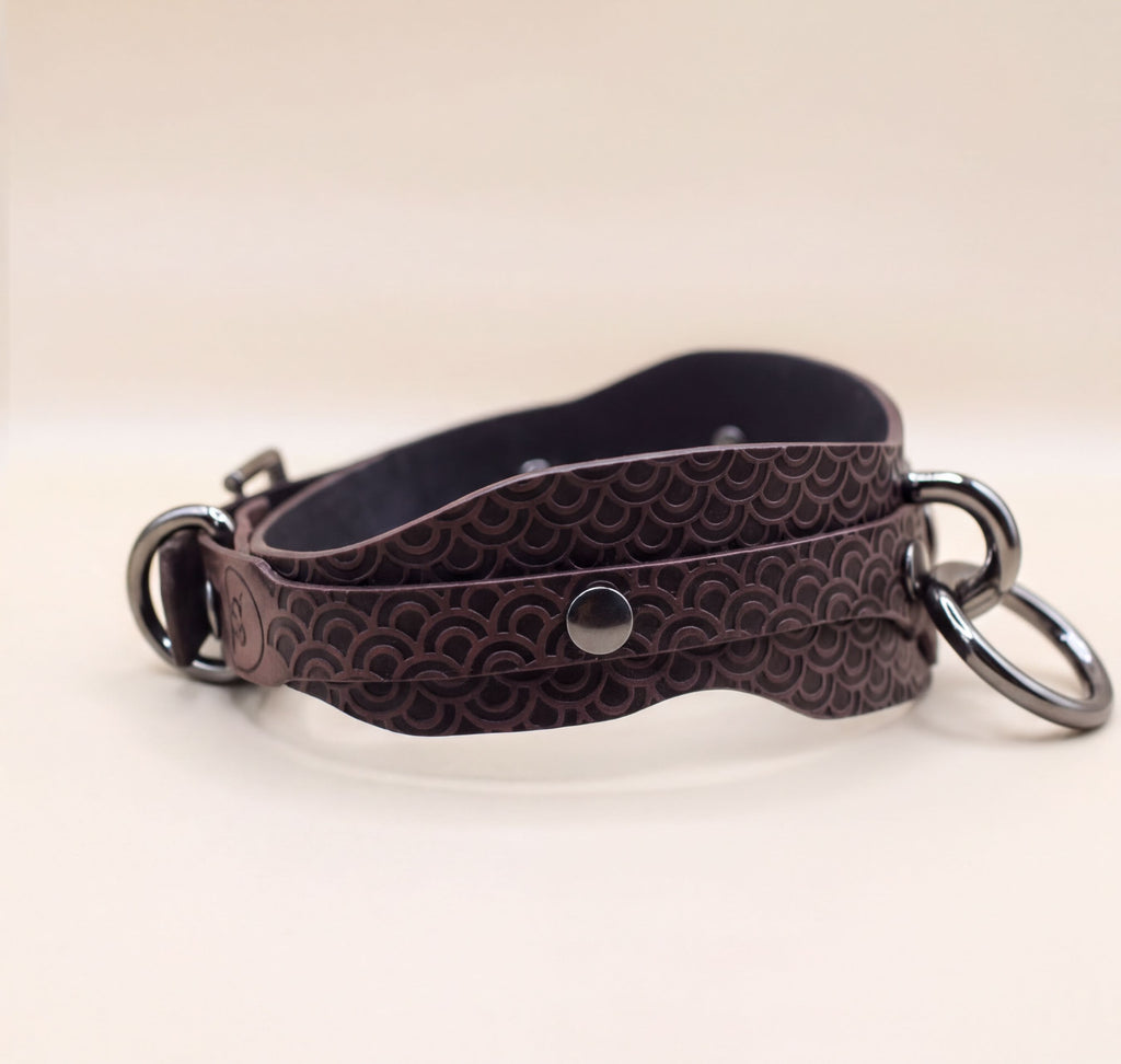 A brown leather strap with a metal buckle and two metal rings attached to it.