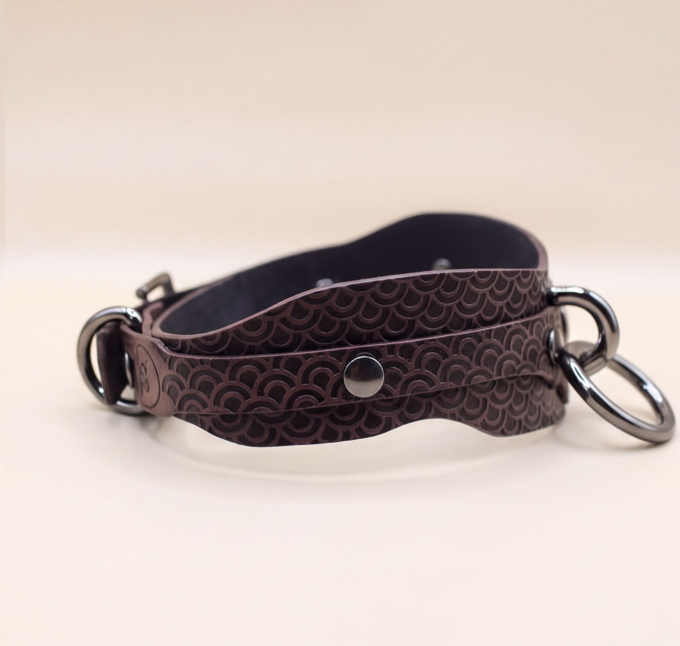 A brown leather strap with a metal buckle and two metal rings attached to it.