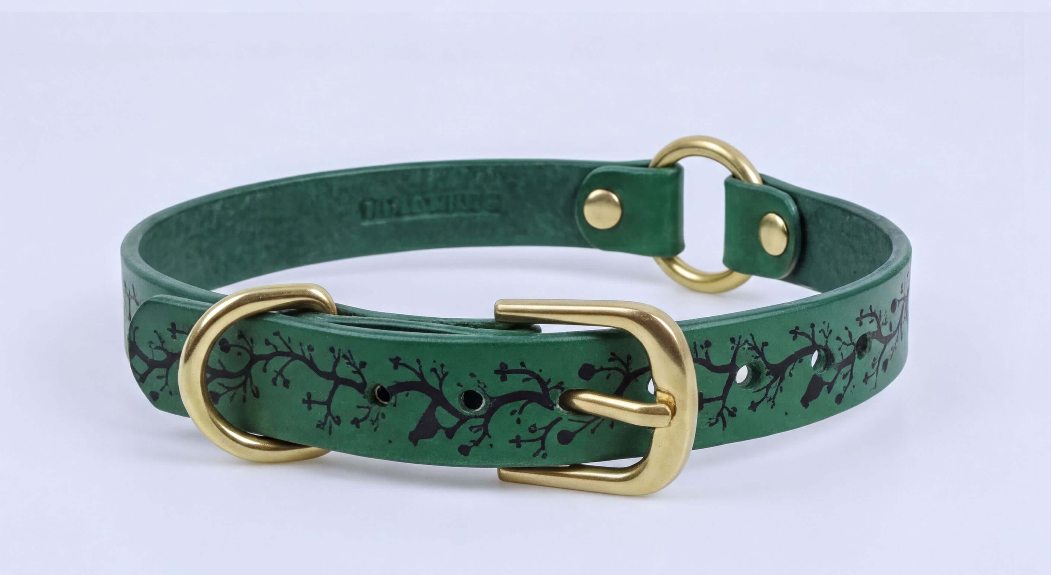 A green leather dog collar with a gold buckle and a tree branch pattern.