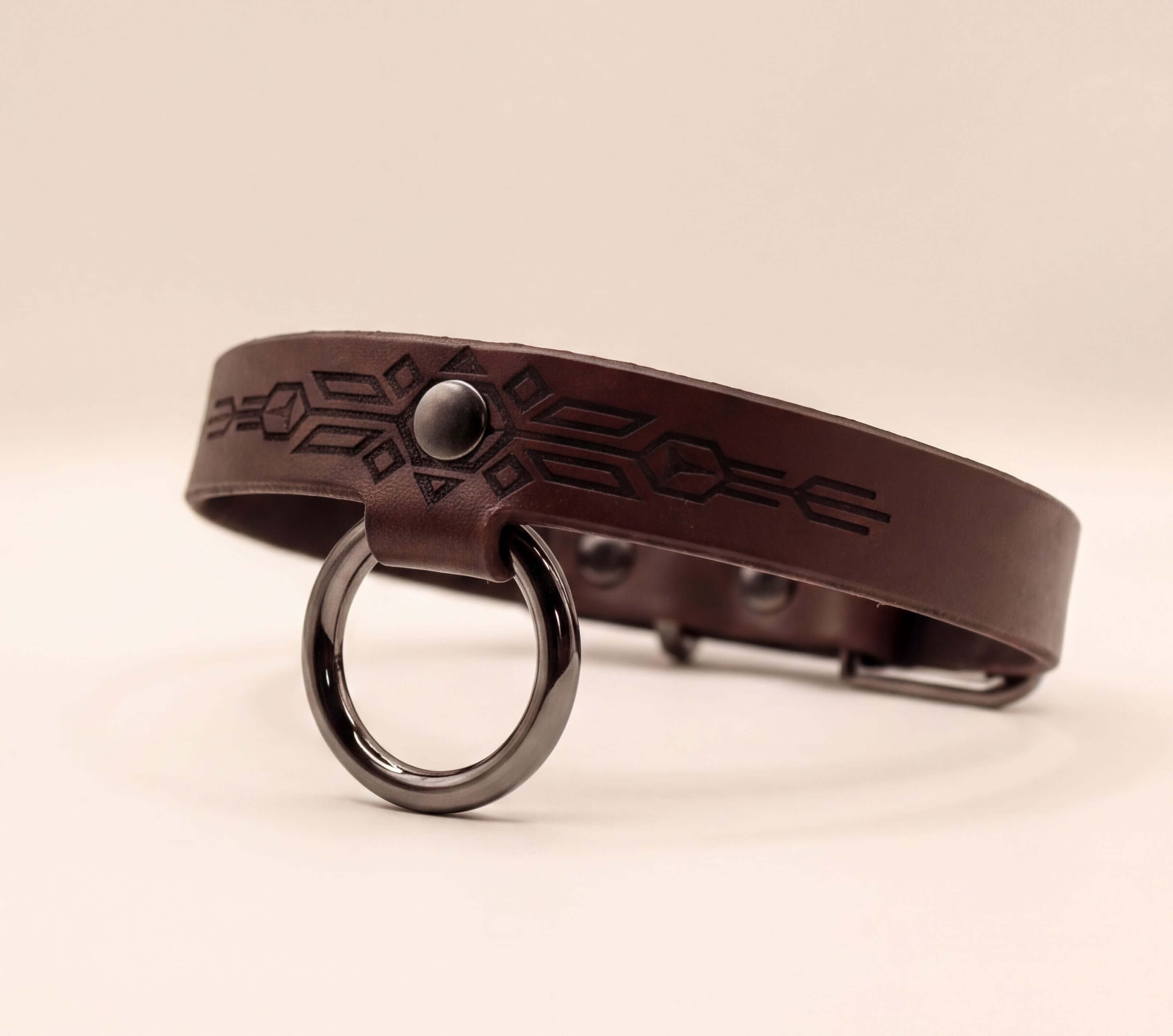 A brown leather collar with a metal ring and a geometric design on the strap.