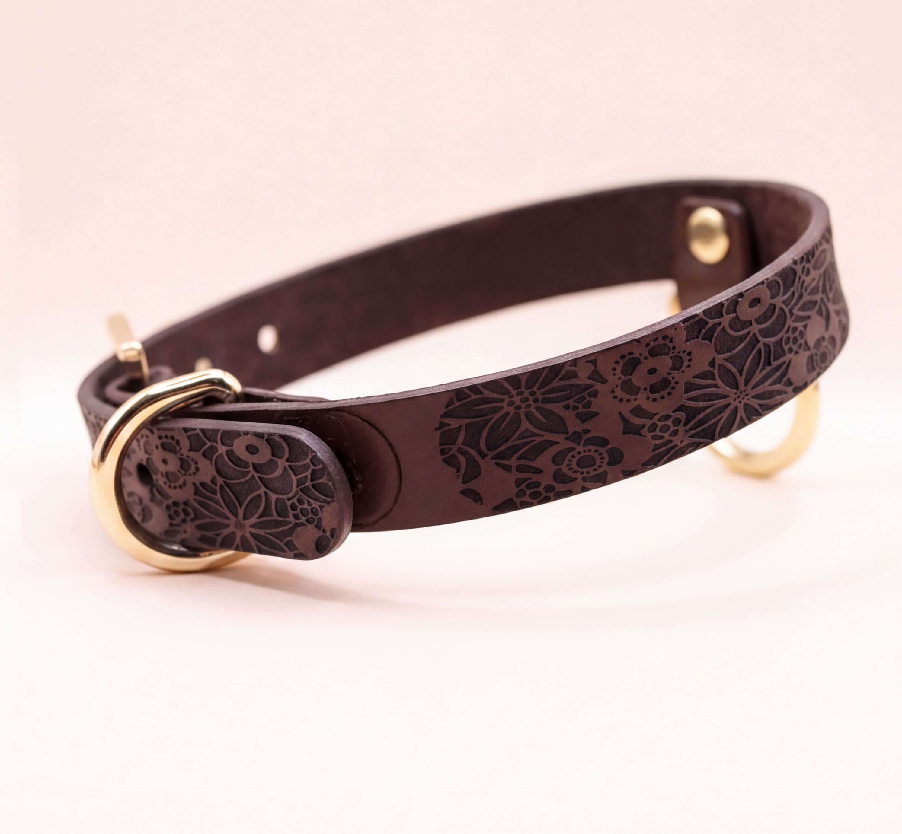A brown leather dog collar with a floral pattern and a gold buckle.