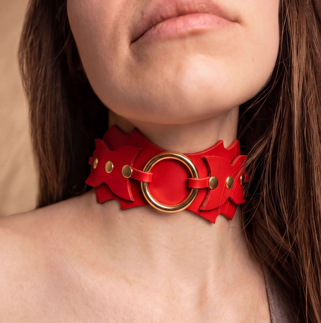 A close-up of a woman's neck wearing a red leather choker necklace with a large circular ring.