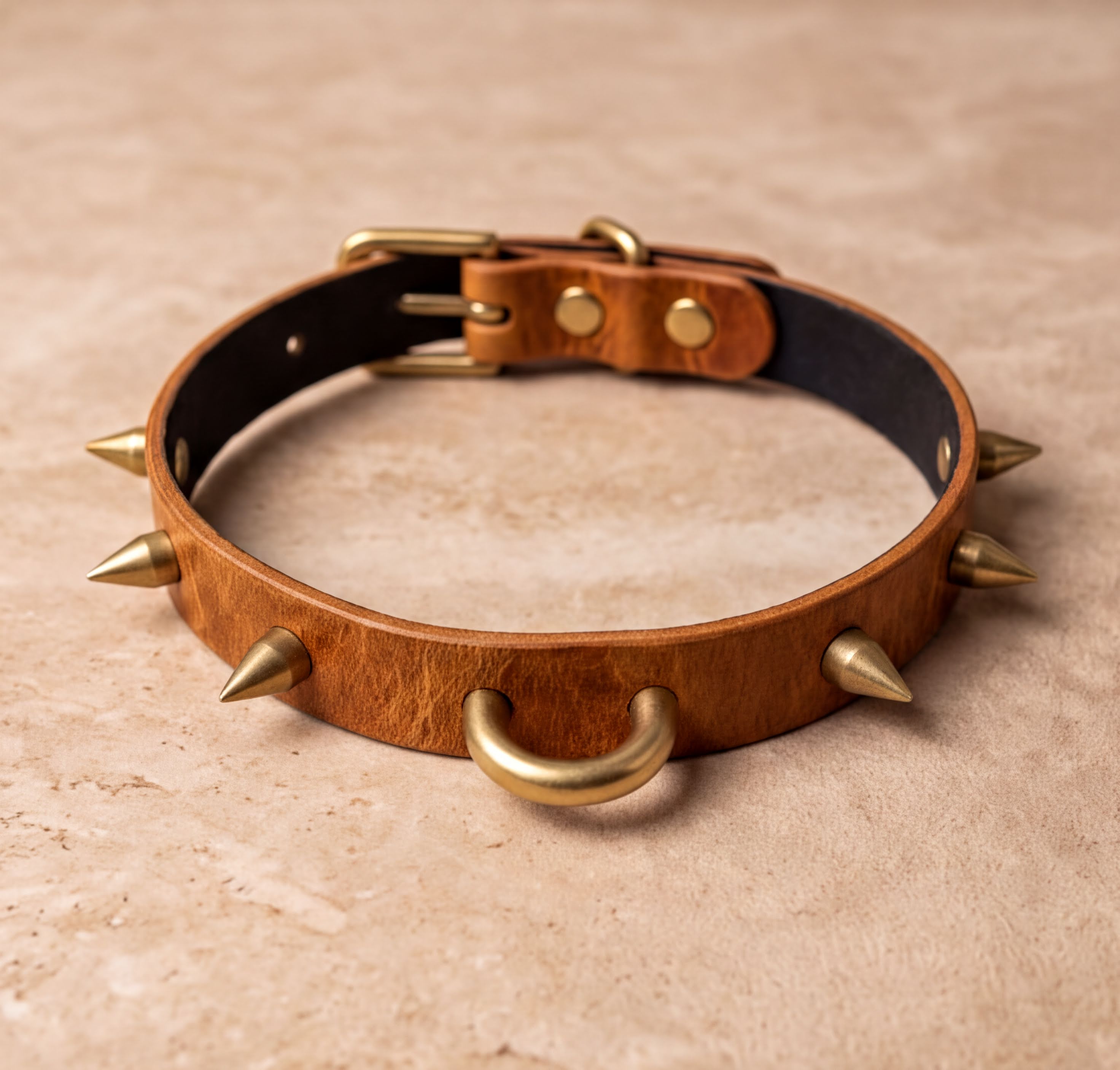 A brown leather dog collar with spikes protruding from it, resting on a beige surface.