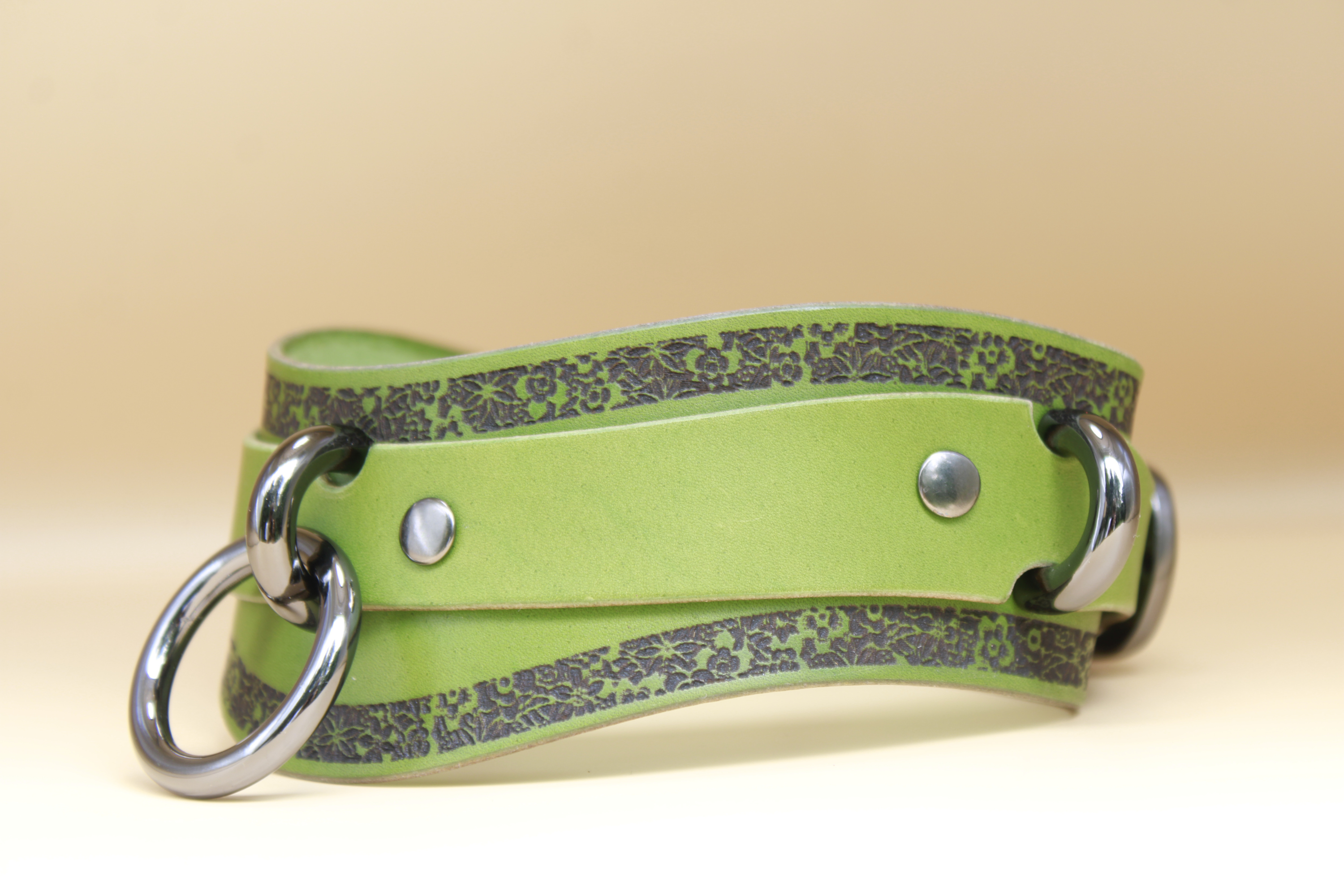 A green leather strap with metal rings and decorative patterns on it.