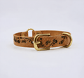 A tan leather dog collar with a floral pattern and two brass buckles.