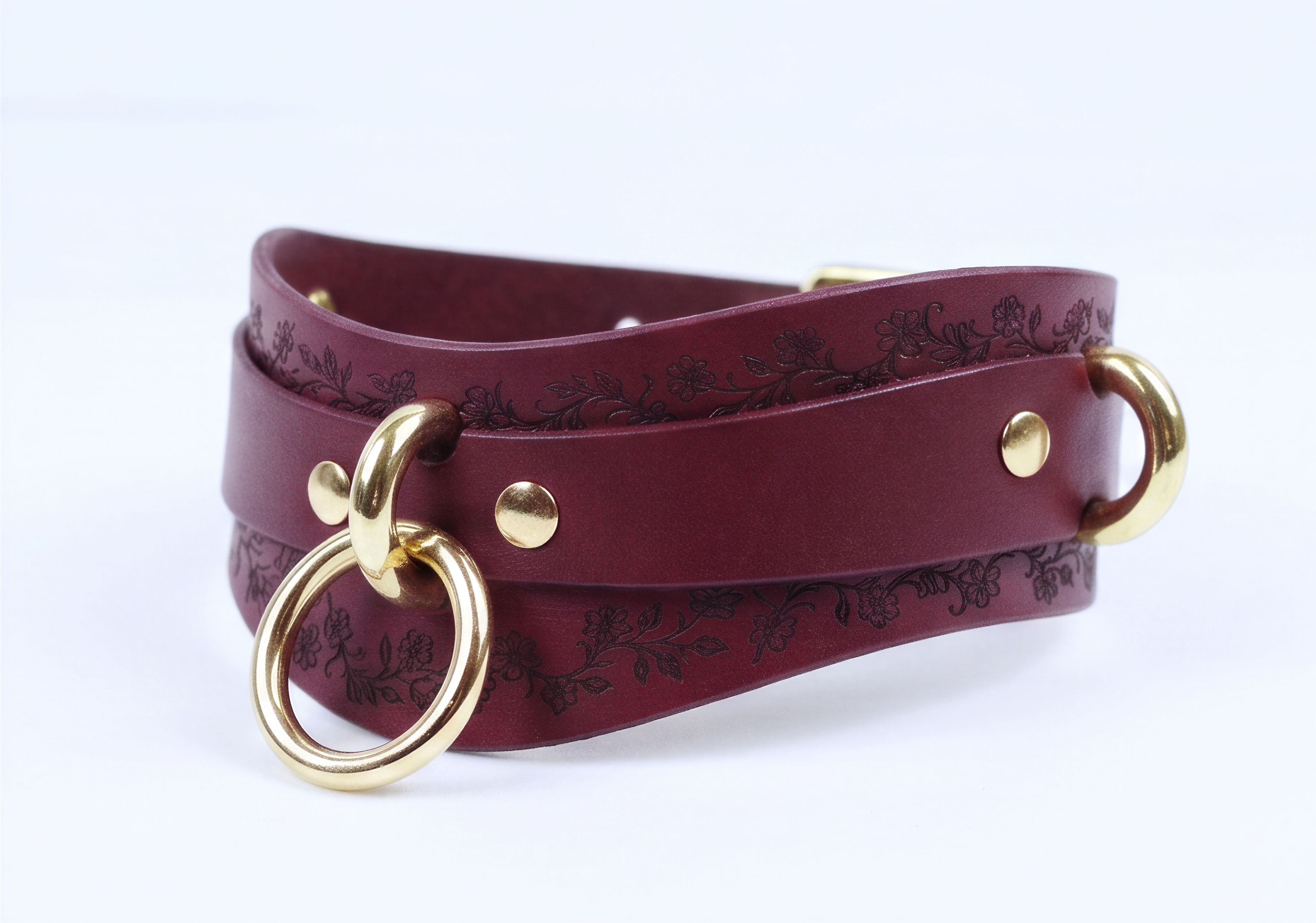 A burgundy leather choker necklace with a gold-colored metal ring and two gold-colored metal rings on either side.