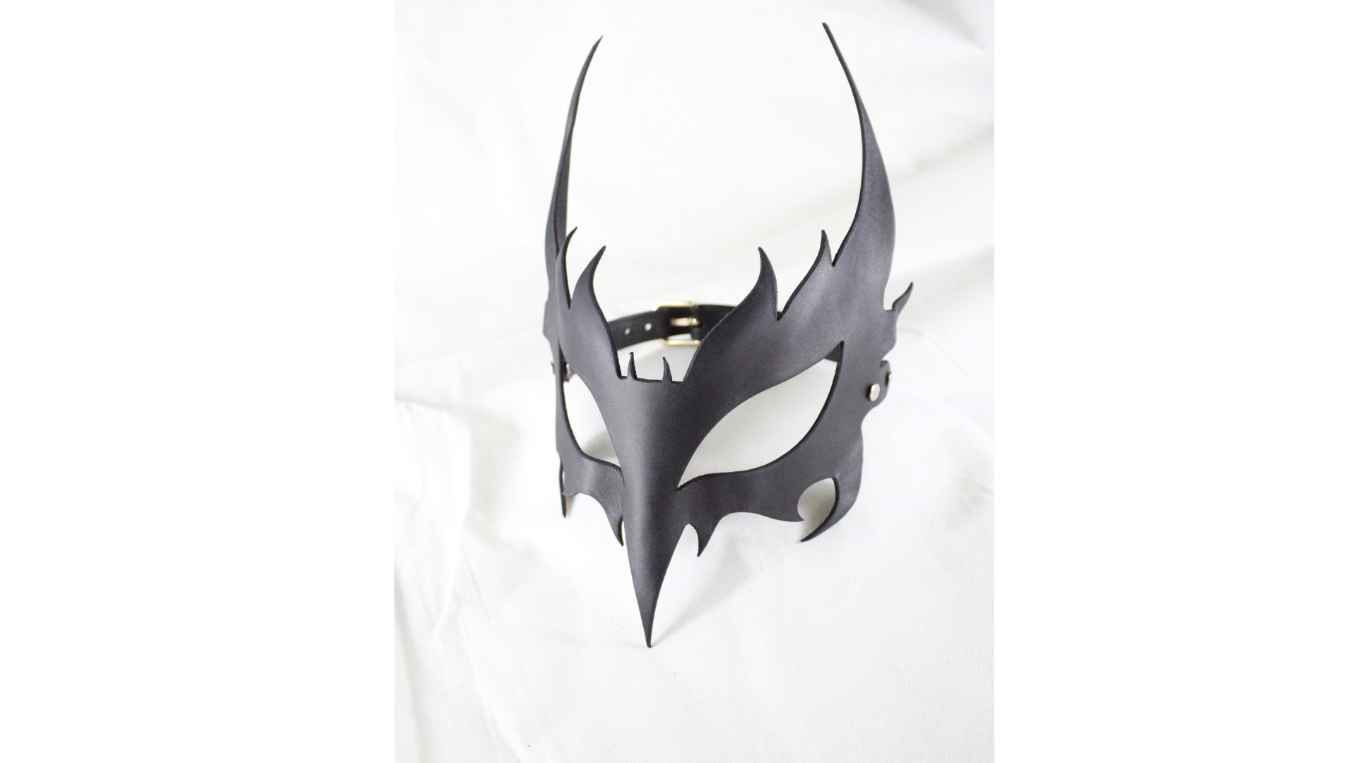 A black mask with sharp, pointed features is displayed against a white background.