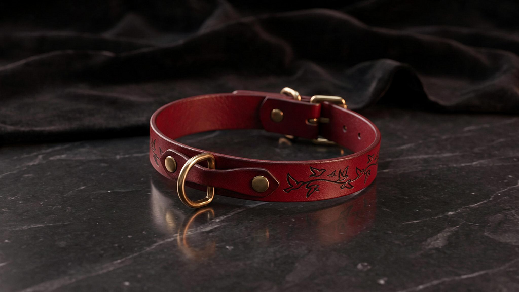 A red leather collar with a gold buckle and a leaf design on the side, resting on a dark surface.
