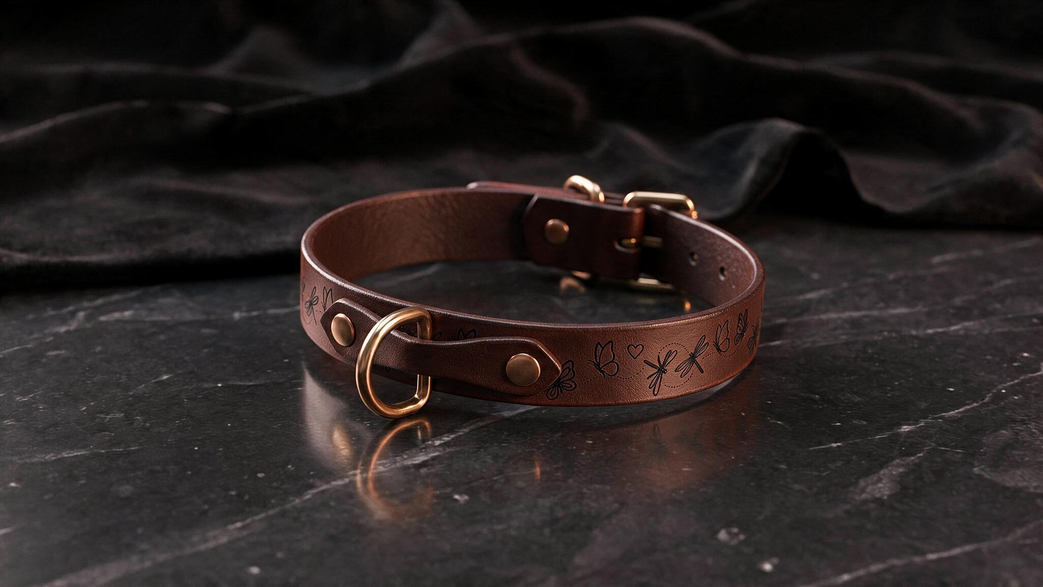 A brown leather collar with a gold-colored buckle and a floral design on the surface.