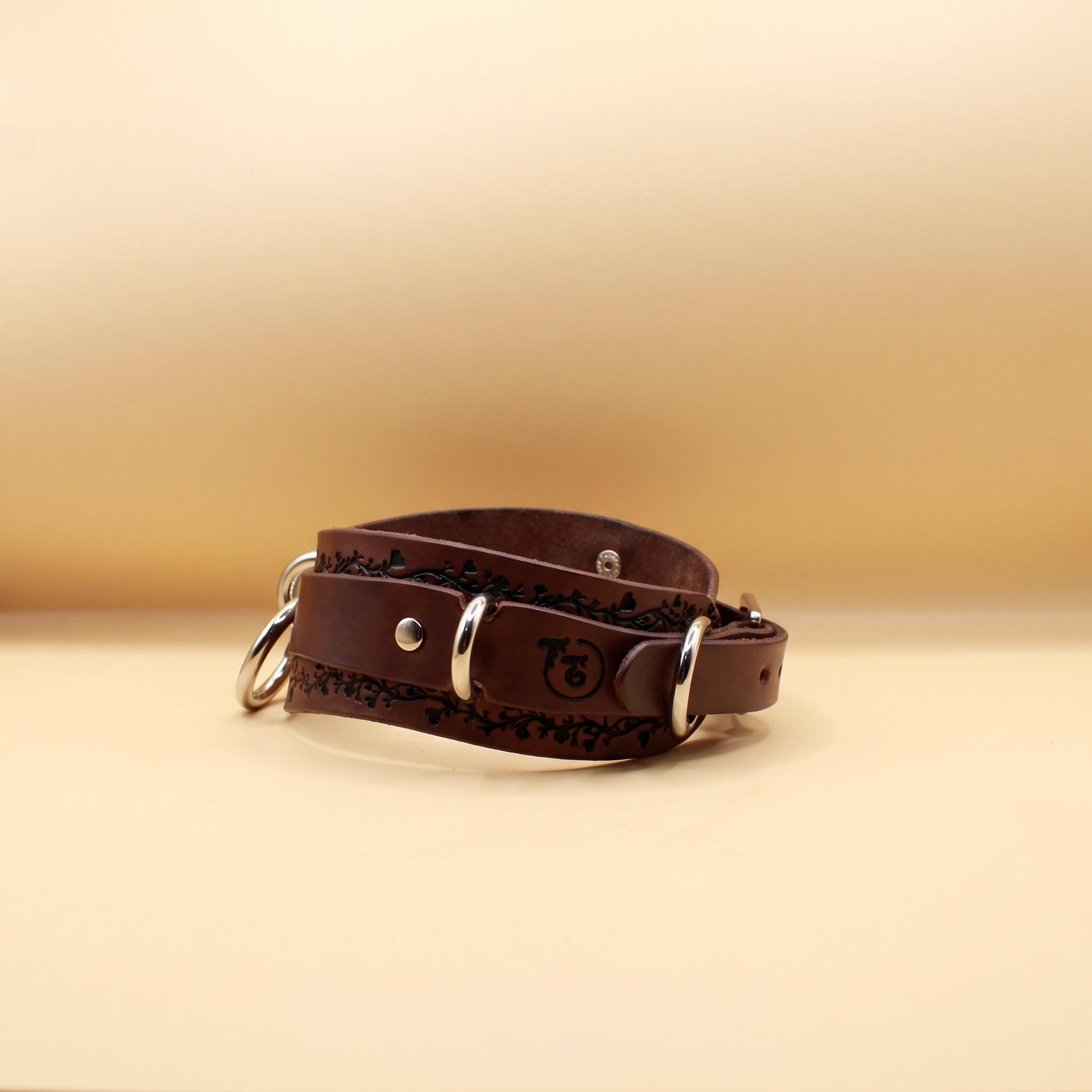 A brown leather dog collar with metal rings and a logo on the front.