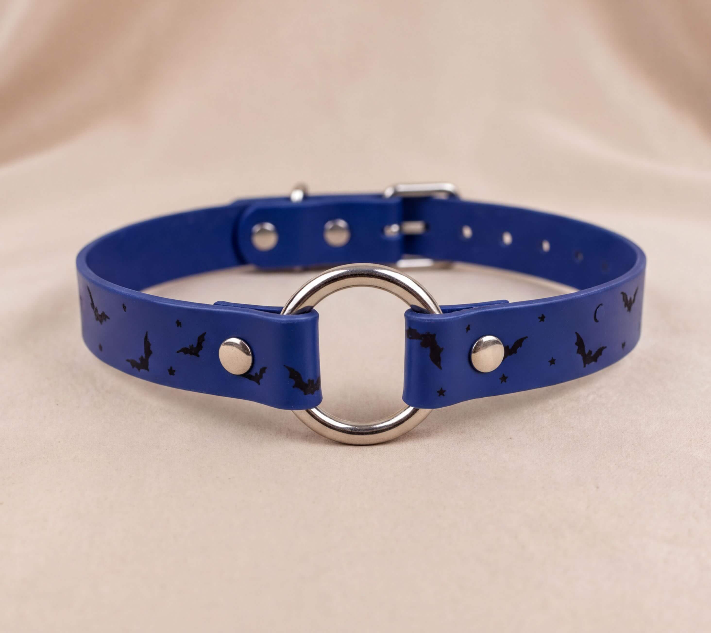 A blue collar with a silver ring and bat designs, featuring a circular metal ring and small black bats.